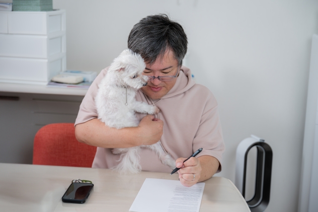 白い小型犬を抱きながら書類に記入する飼い主