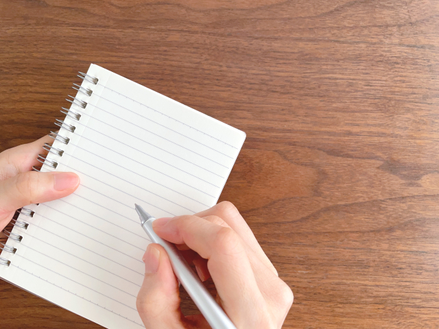 木製のテーブルでノートに書き込む手